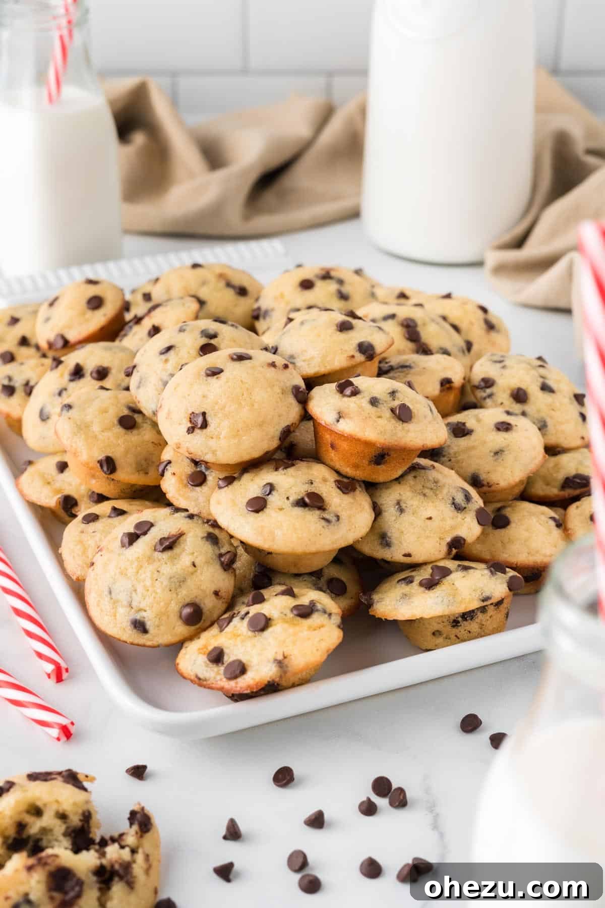 A generous stack of golden-brown mini chocolate chip muffins on a white platter, ready to be served.