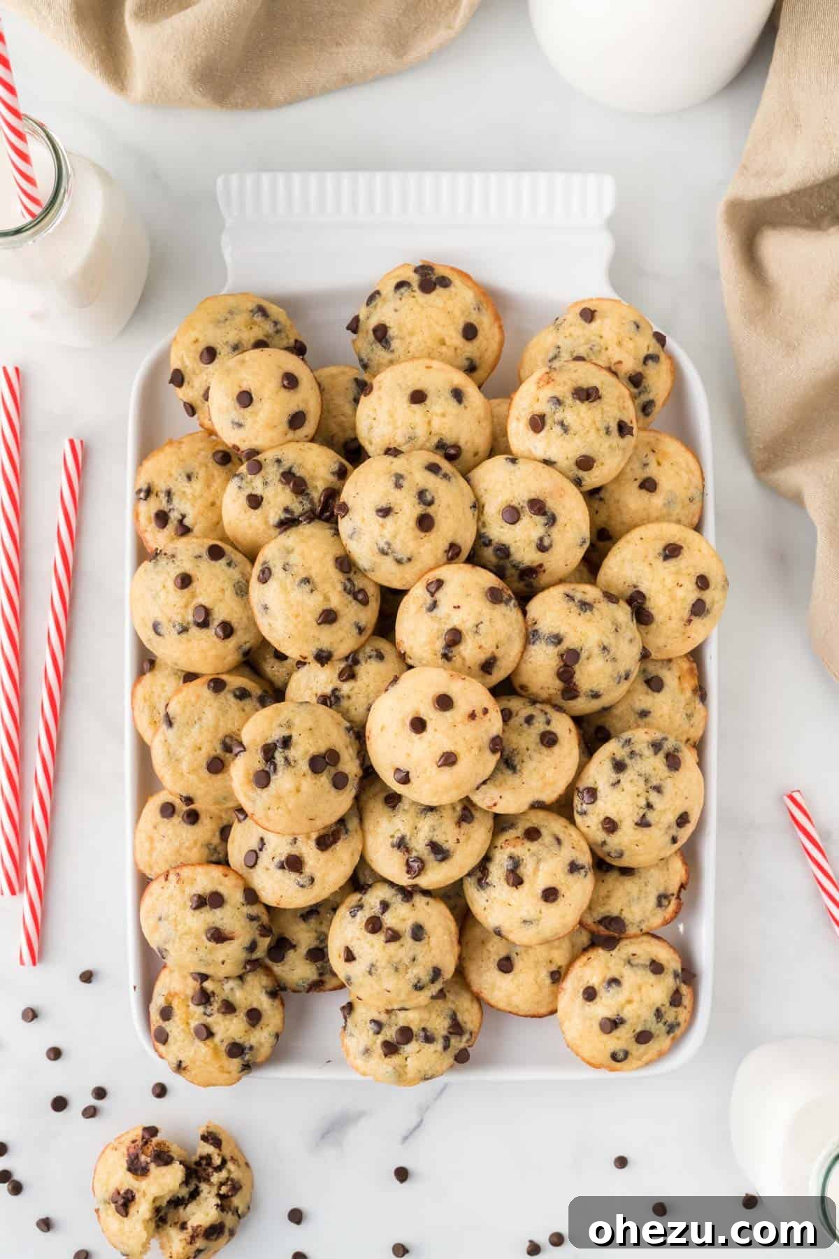 Numerous mini chocolate chip muffins piled high on a white serving platter.