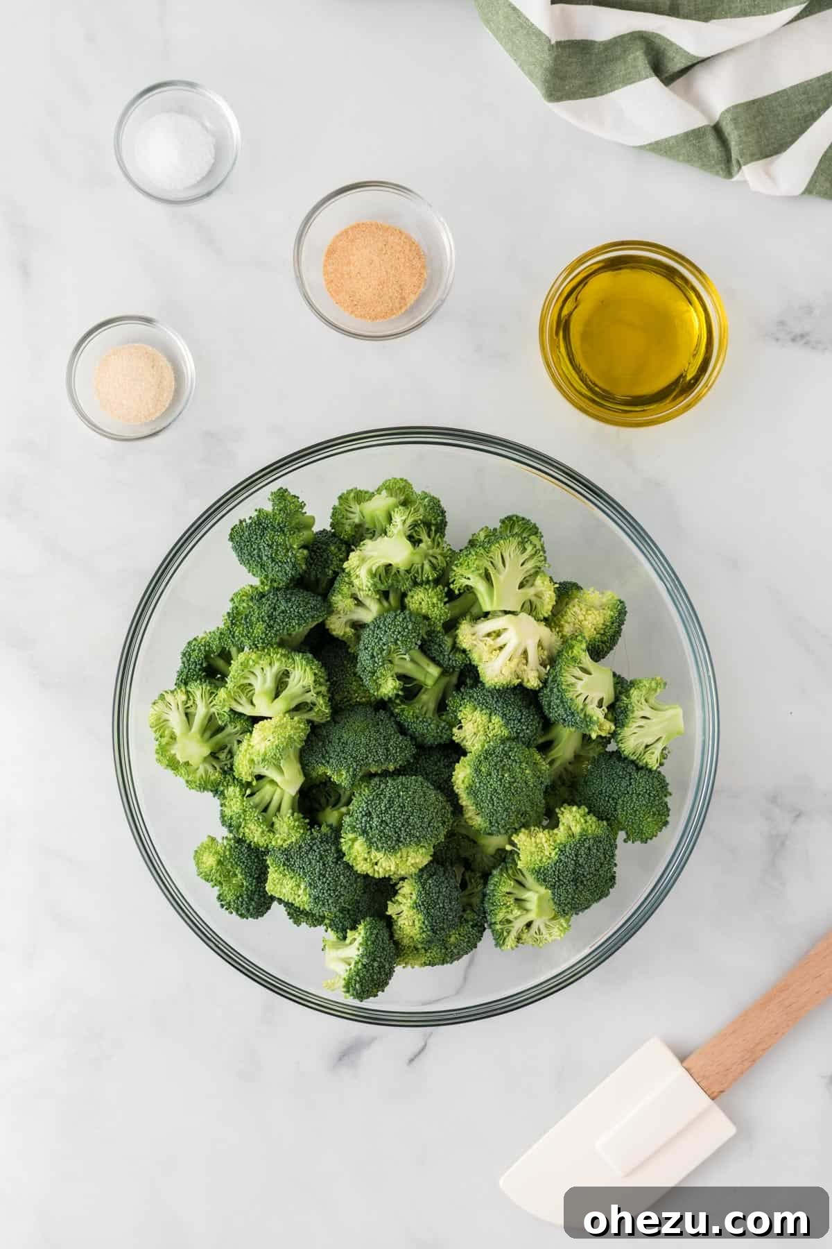 Crispy Parmesan Roasted Broccoli 5 Broccoli florets in a large mixing bowl, drizzled with olive oil and sprinkled with salt, garlic powder, and onion powder, ready for tossing