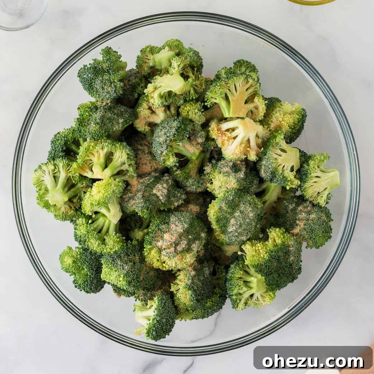 Crispy Parmesan Roasted Broccoli 6 Hands tossing fresh broccoli florets with olive oil and spices in a large mixing bowl to ensure even coating