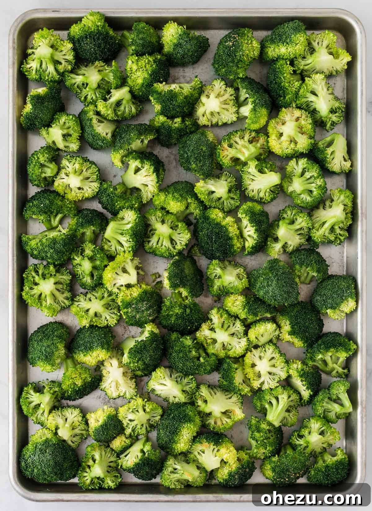Crispy Parmesan Roasted Broccoli 8 Partially roasted broccoli florets spread on a baking sheet, with some browning on the edges, before the addition of parmesan