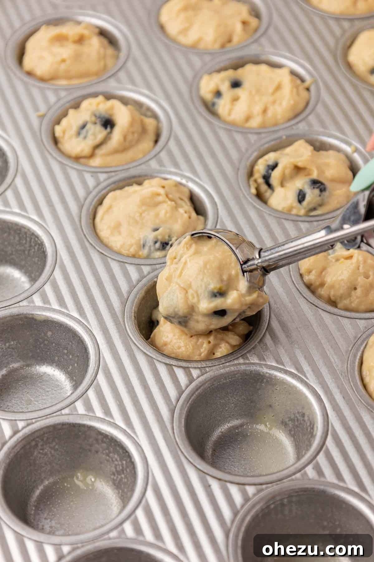 Blueberry Poppers 13 Scooping blueberry muffin batter into a greased mini muffin tin.