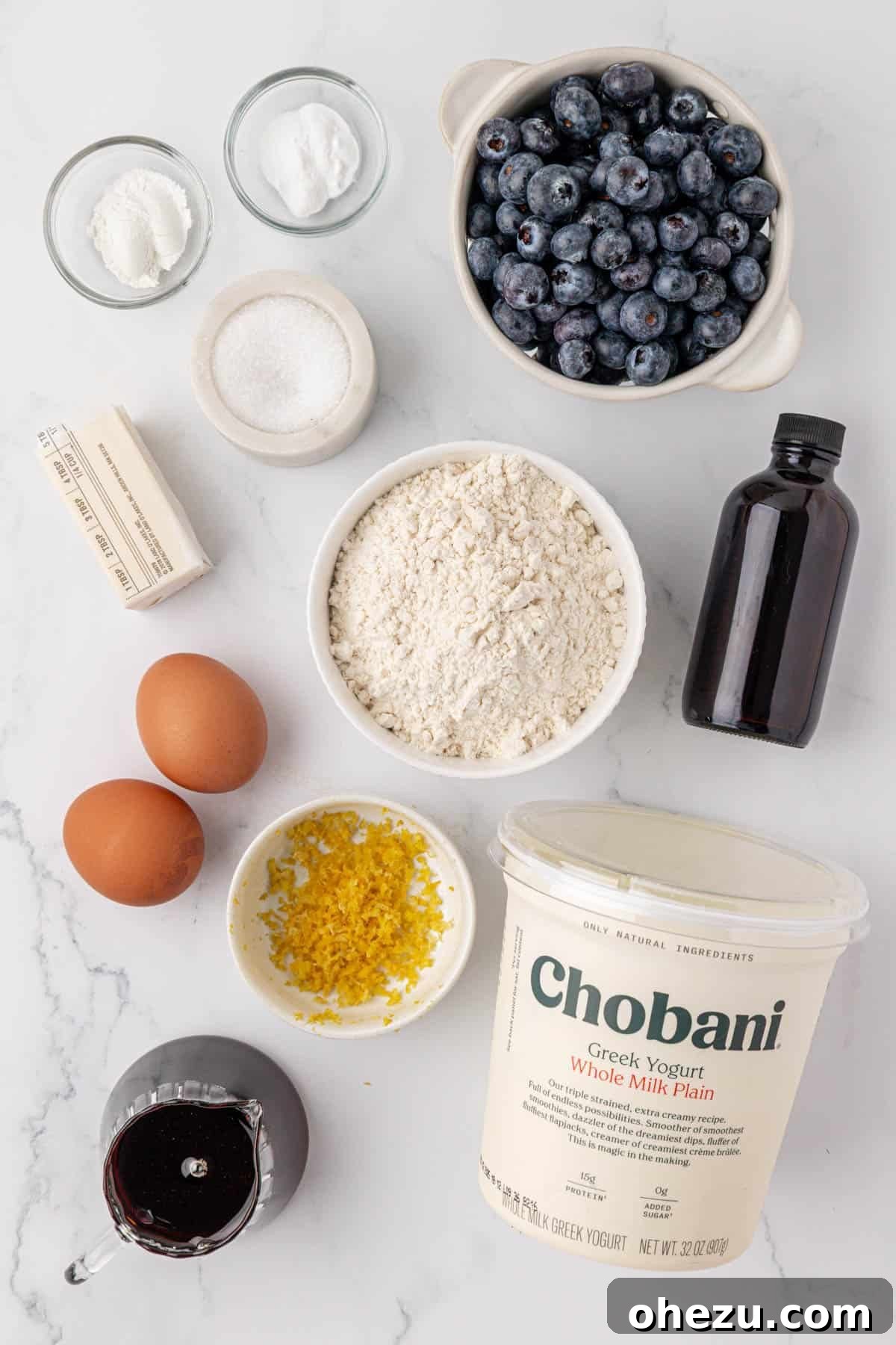 Blueberry Poppers 4 Assortment of fresh ingredients laid out on a counter, including Greek yogurt, blueberries, eggs, flour, and lemon, ready for making mini muffins.