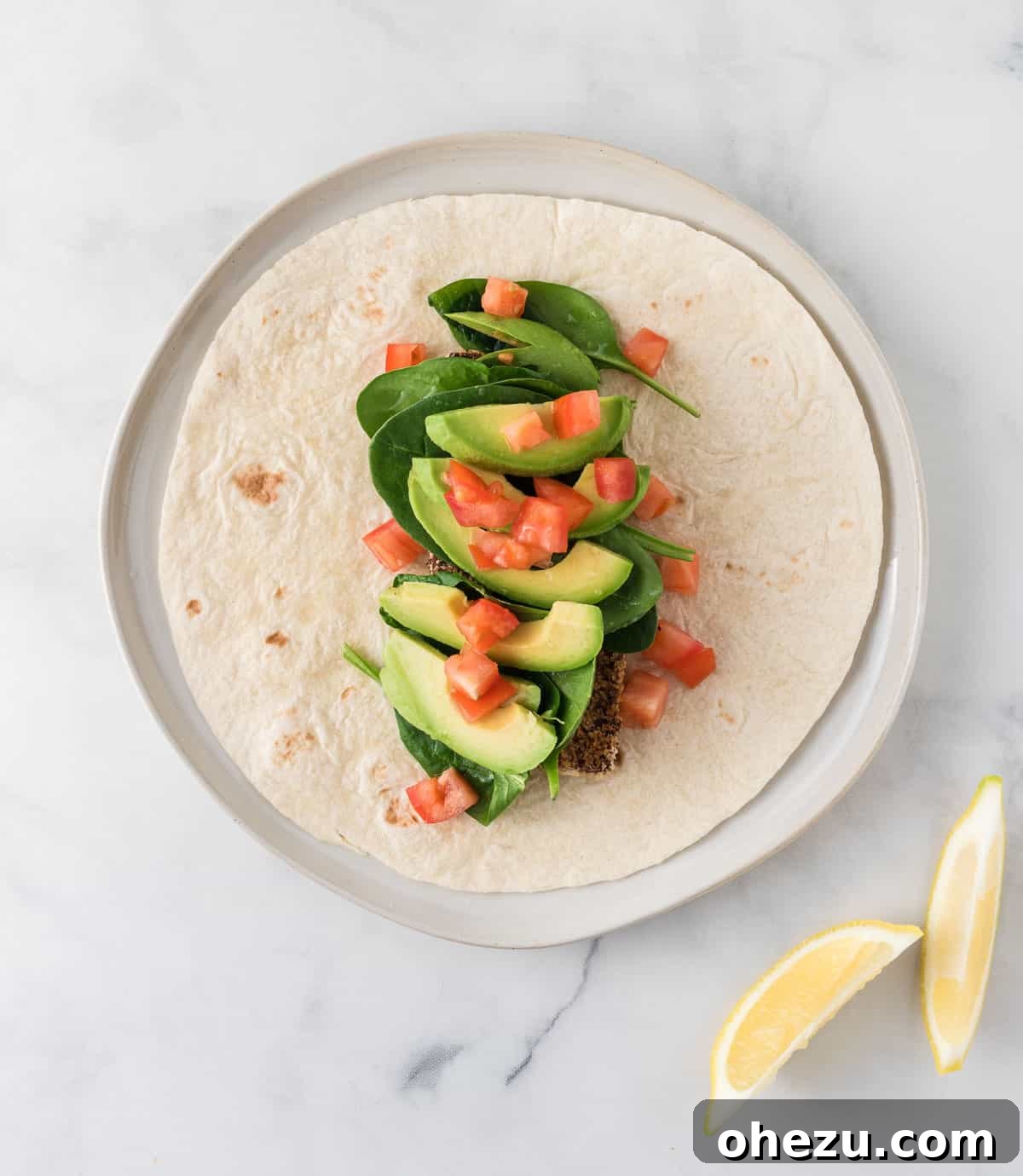 Vibrant Tofu Wraps 15 An assembled tofu wrap, showcasing the layers of crispy tofu, fresh spinach, creamy avocado, ripe tomato, and a bright lemon wedge, before being rolled.