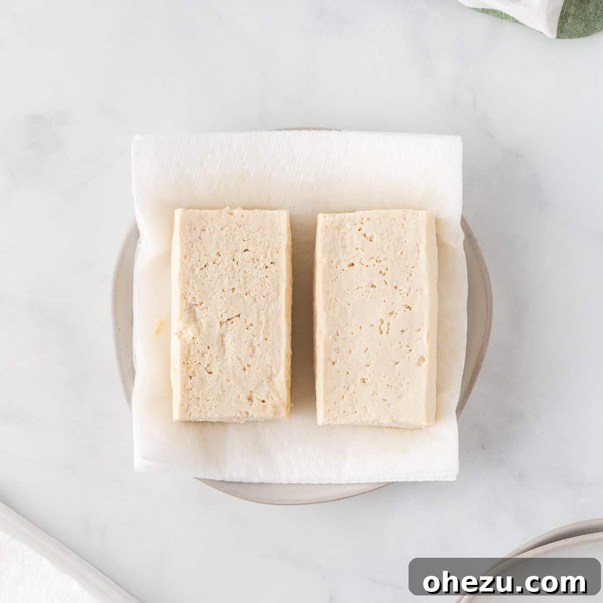 Vibrant Tofu Wraps 6 Two blocks of thawed and pressed tofu resting on a paper towel-lined plate, having released excess liquid.