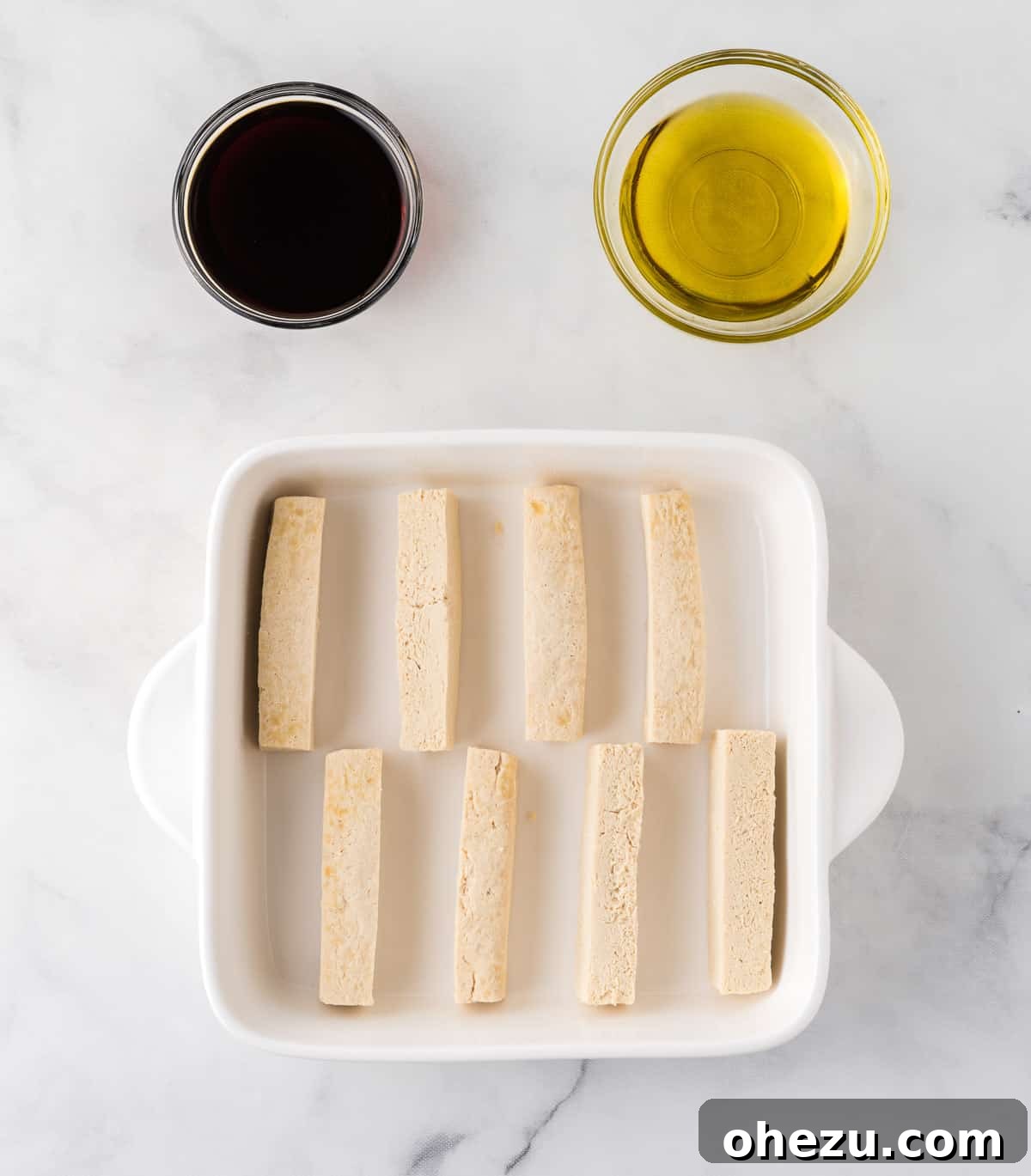 Vibrant Tofu Wraps 8 Tofu strips arranged in a baking dish, with olive oil and soy sauce being drizzled over them for marination.