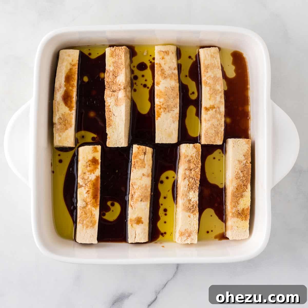 Vibrant Tofu Wraps 9 Close-up of tofu strips marinating in soy sauce and olive oil within a glass baking dish, showing liquid absorption.