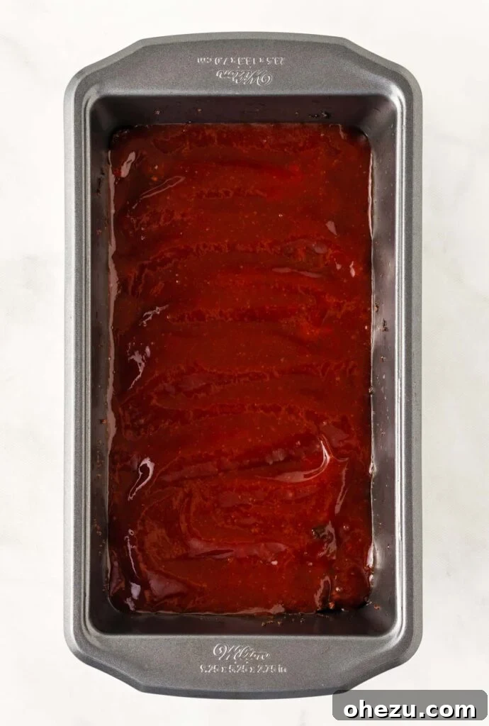 Meatless Meatloaf Marvel 14 A vegetarian meatloaf in a loaf pan, partially baked and generously topped with a rich, glossy brown sugar and ketchup glaze, ready for its final bake.