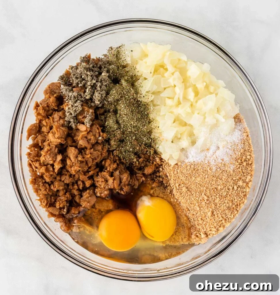 Meatless Meatloaf Marvel 8 A large mixing bowl filled with various vegetarian meatloaf ingredients, including thawed crumbles, eggs, breadcrumbs, and seasonings, poised for thorough mixing.