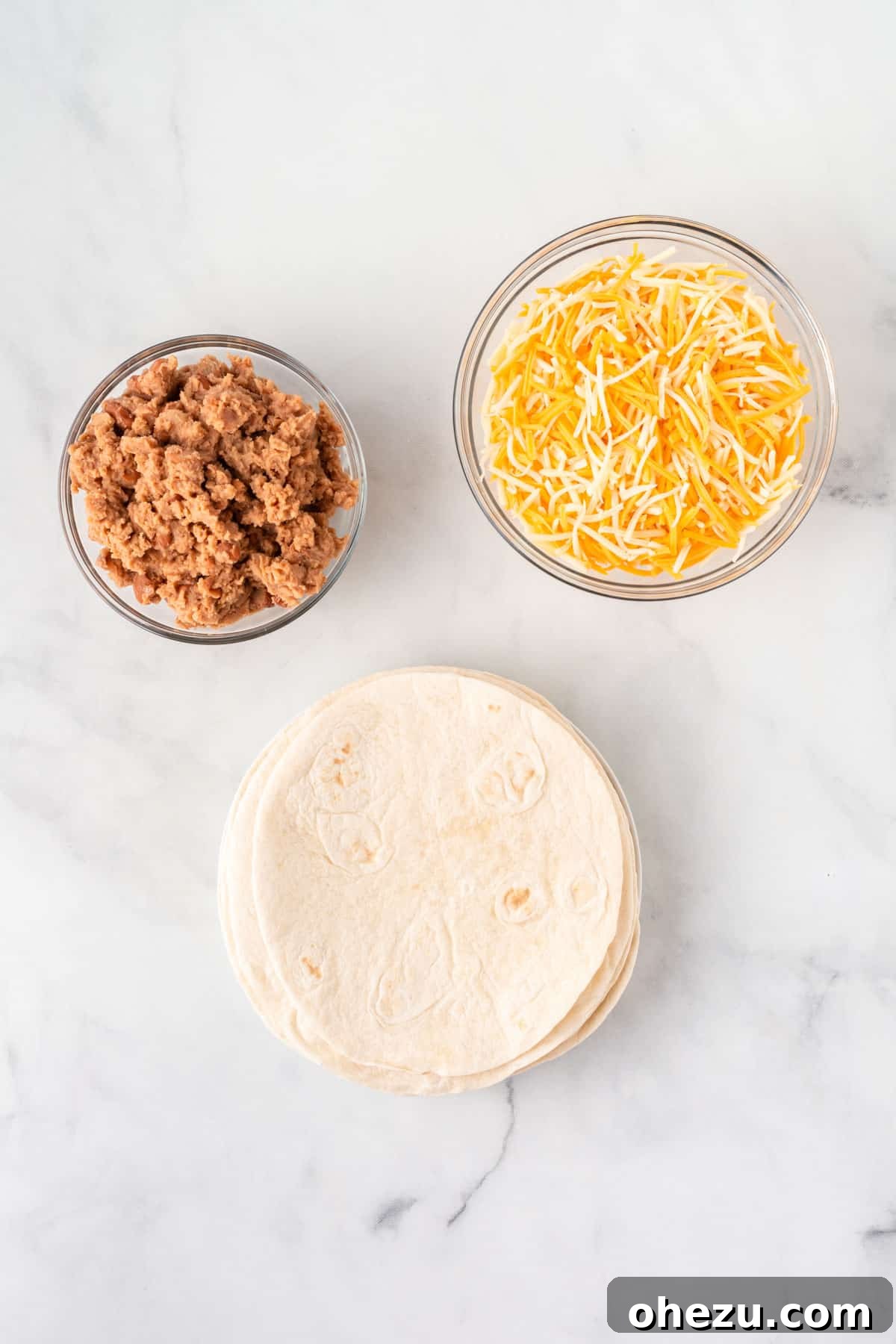 A visual display of the simple ingredients needed for air fryer quesadillas: soft taco shells, creamy refried beans, and a bag of shredded Mexican cheese.