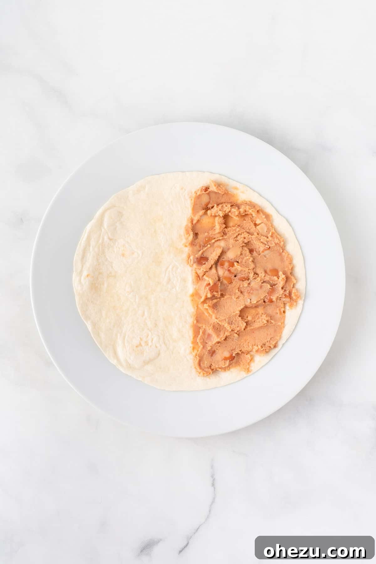 A soft taco shell with refried beans spread evenly over one half, ready for cheese.