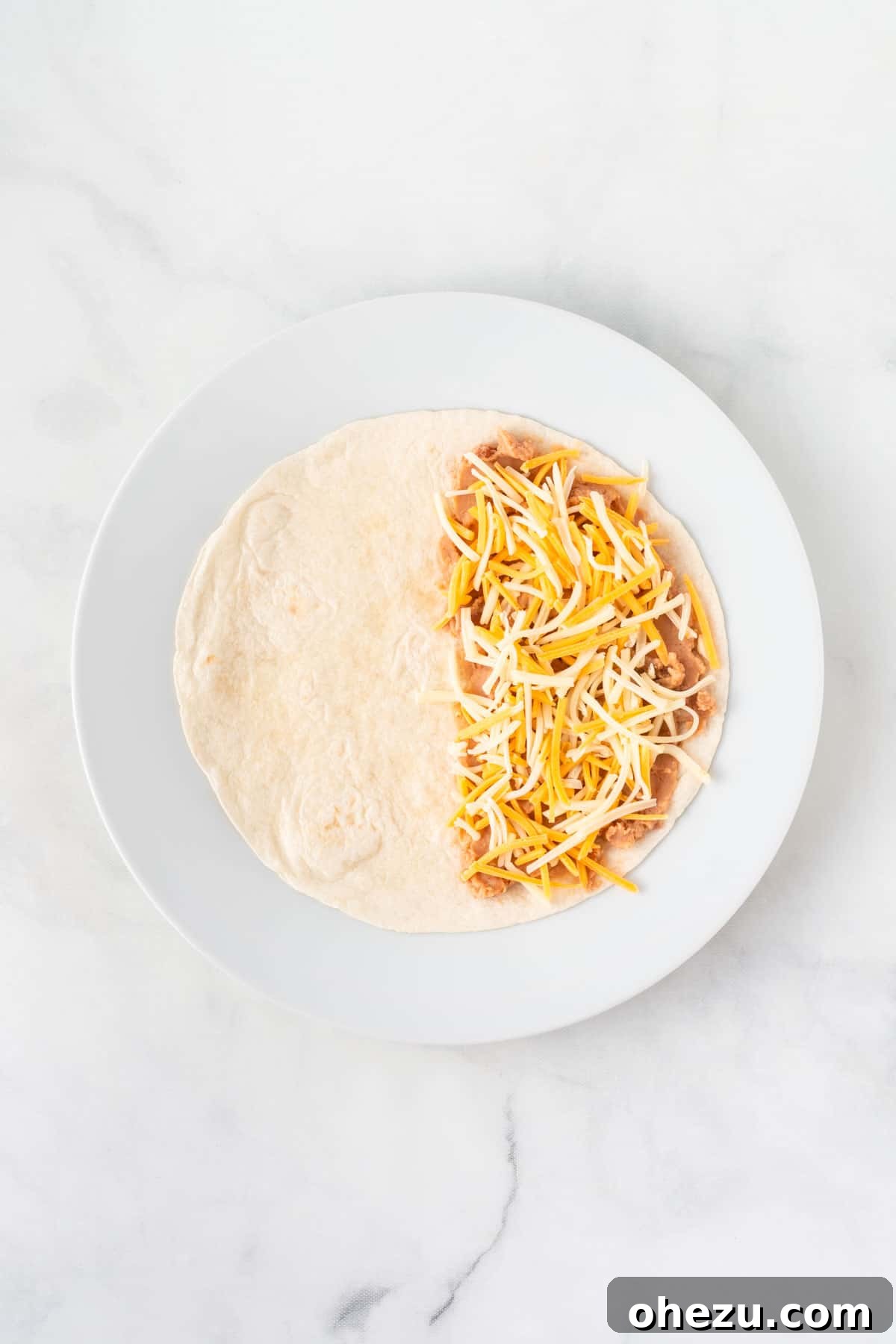 A soft taco shell with refried beans and shredded Mexican cheese covering one half, ready to be folded.