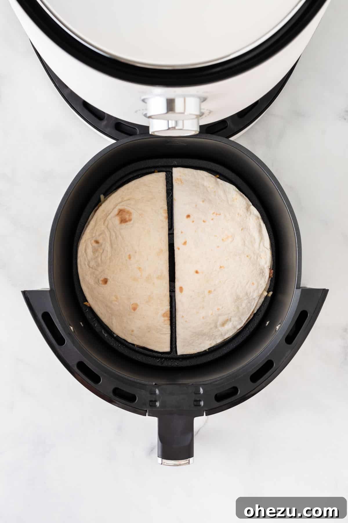 Two folded quesadillas carefully placed side by side in an air fryer basket, ready for cooking.
