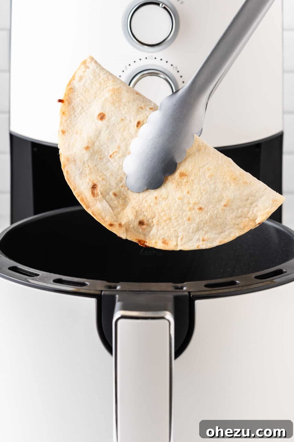 Kitchen tongs carefully removing a hot, crispy quesadilla from the air fryer basket.