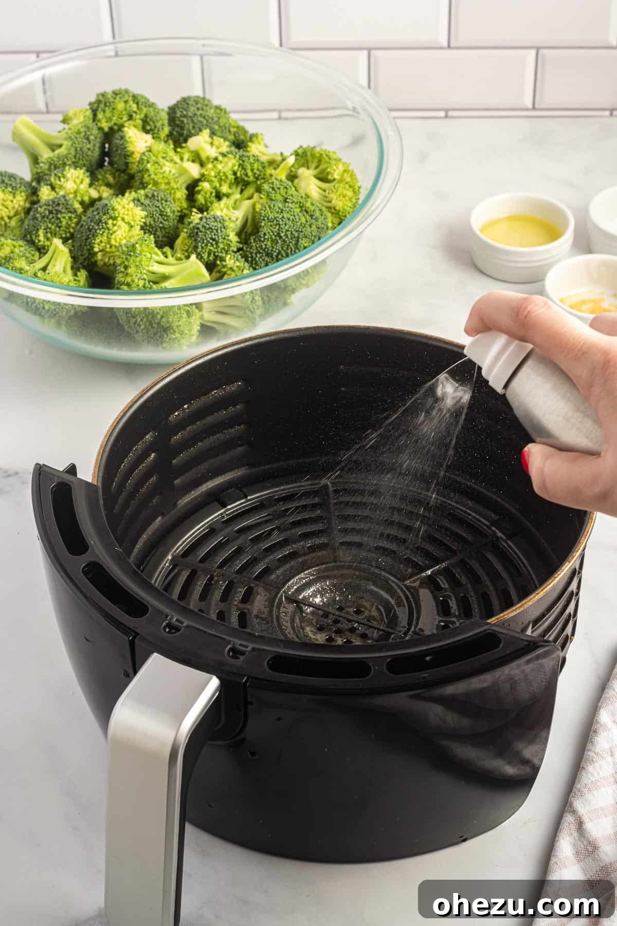 spraying olive oil spray into an air fryer basket