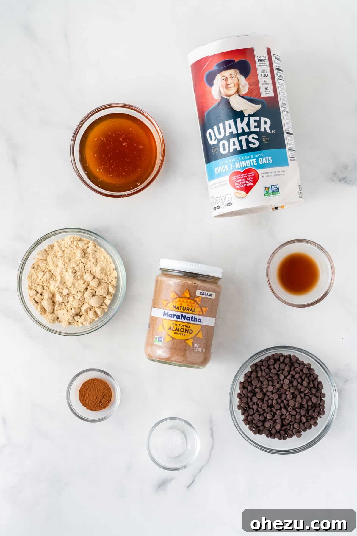 Wholesome Almond Butter Protein Bites 4 A collection of ingredients artfully arranged on a kitchen counter: creamy almond butter, vanilla protein powder, honey, quick oats, mini chocolate chips, salt, cinnamon, and vanilla extract, ready for mixing.