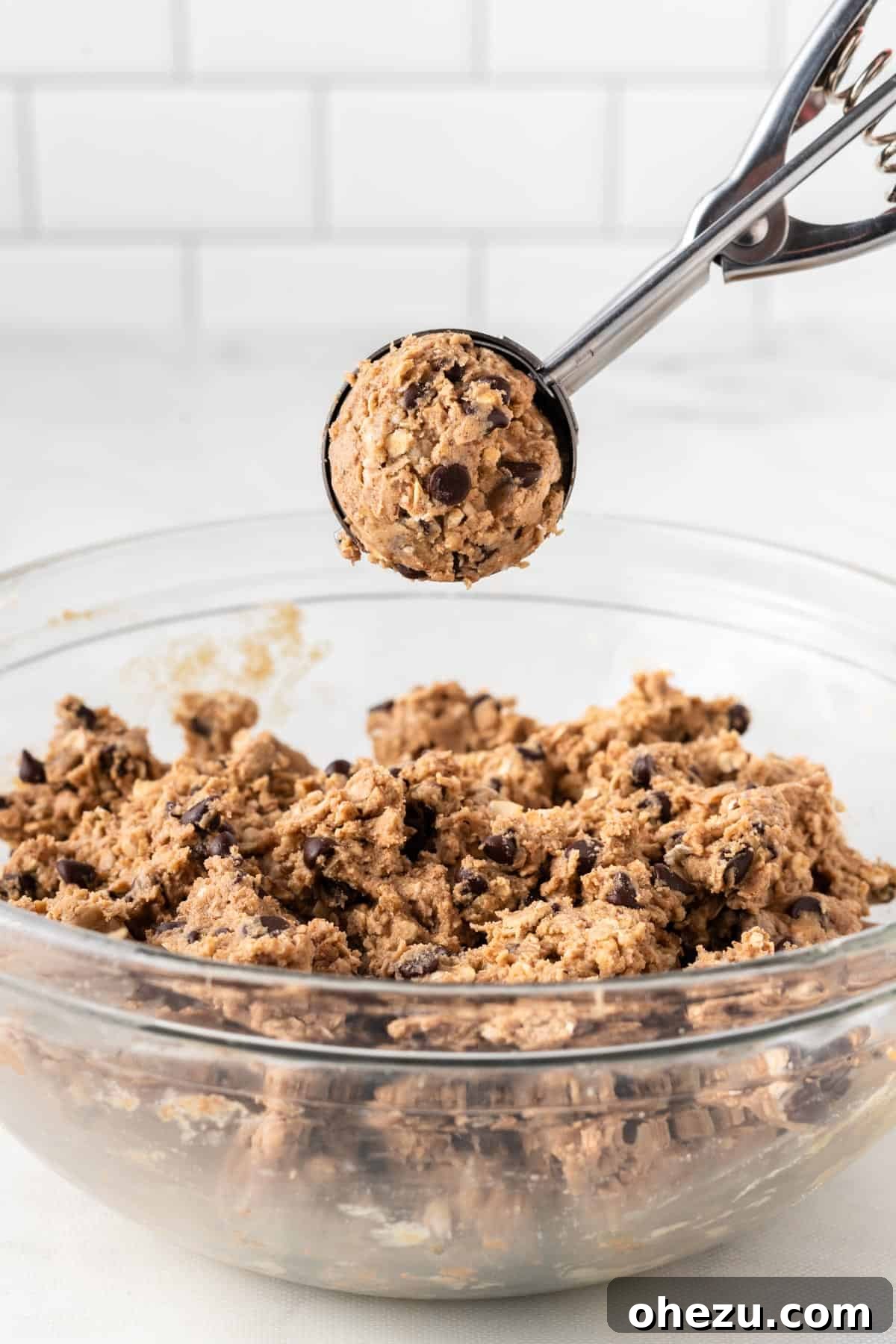 Wholesome Almond Butter Protein Bites 6 A mini cookie scoop filled with almond butter energy ball batter, perfectly portioned and ready to be placed on a baking sheet.