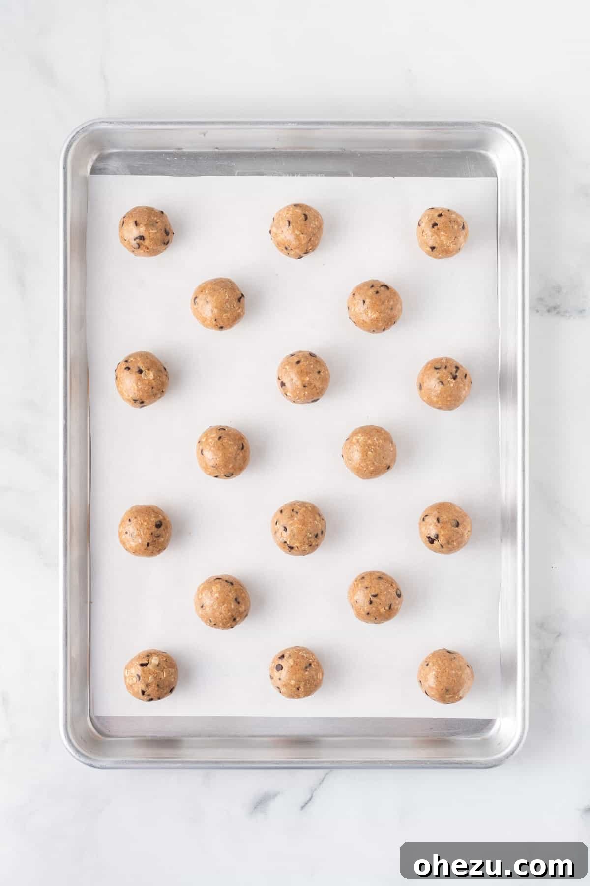 Wholesome Almond Butter Protein Bites 8 Chilled almond butter energy balls on a parchment paper-lined baking sheet, some already rolled smooth, others retaining their initial scooped shape.
