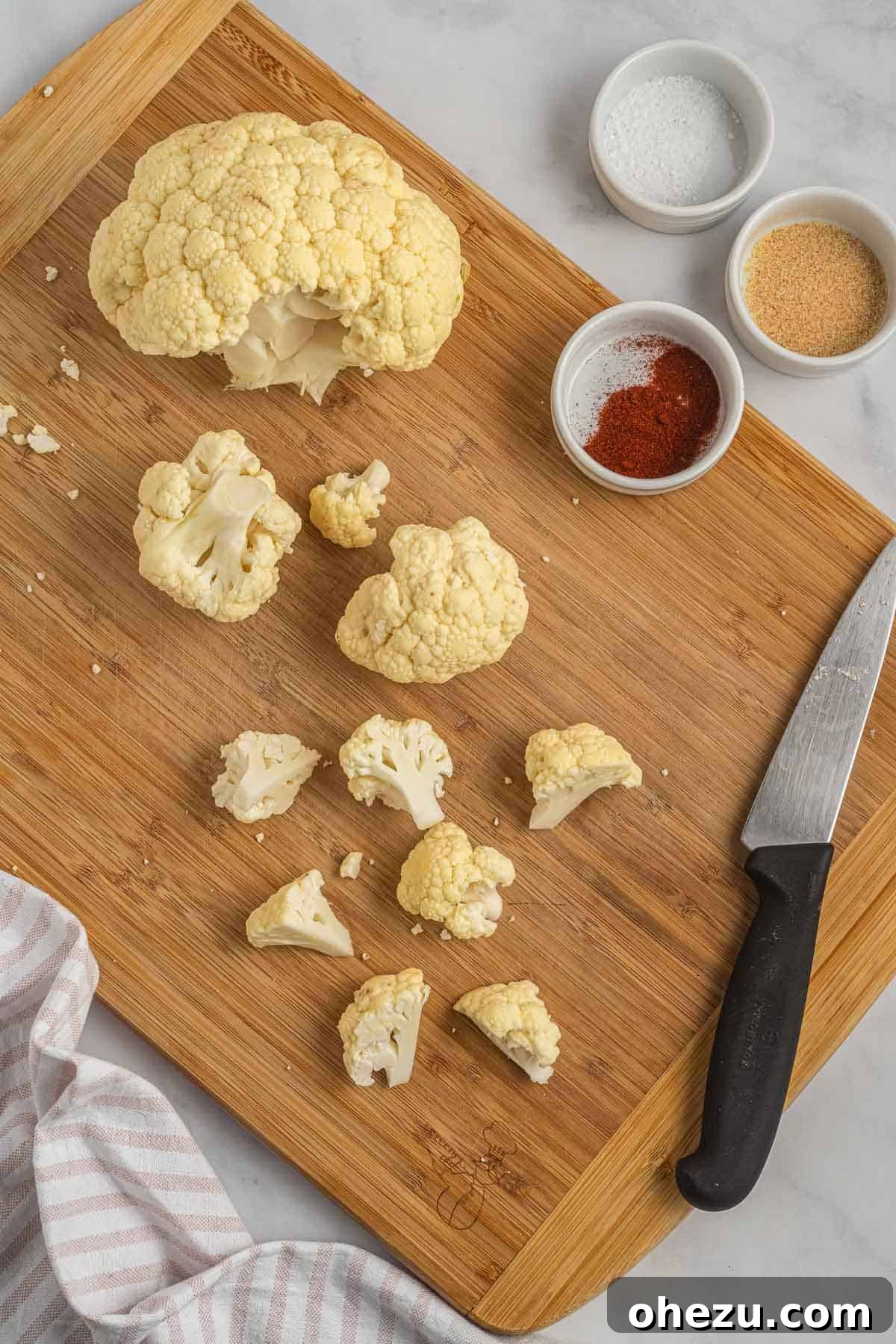 A person's hands cutting a head of cauliflower into small, uniform florets on a cutting board.