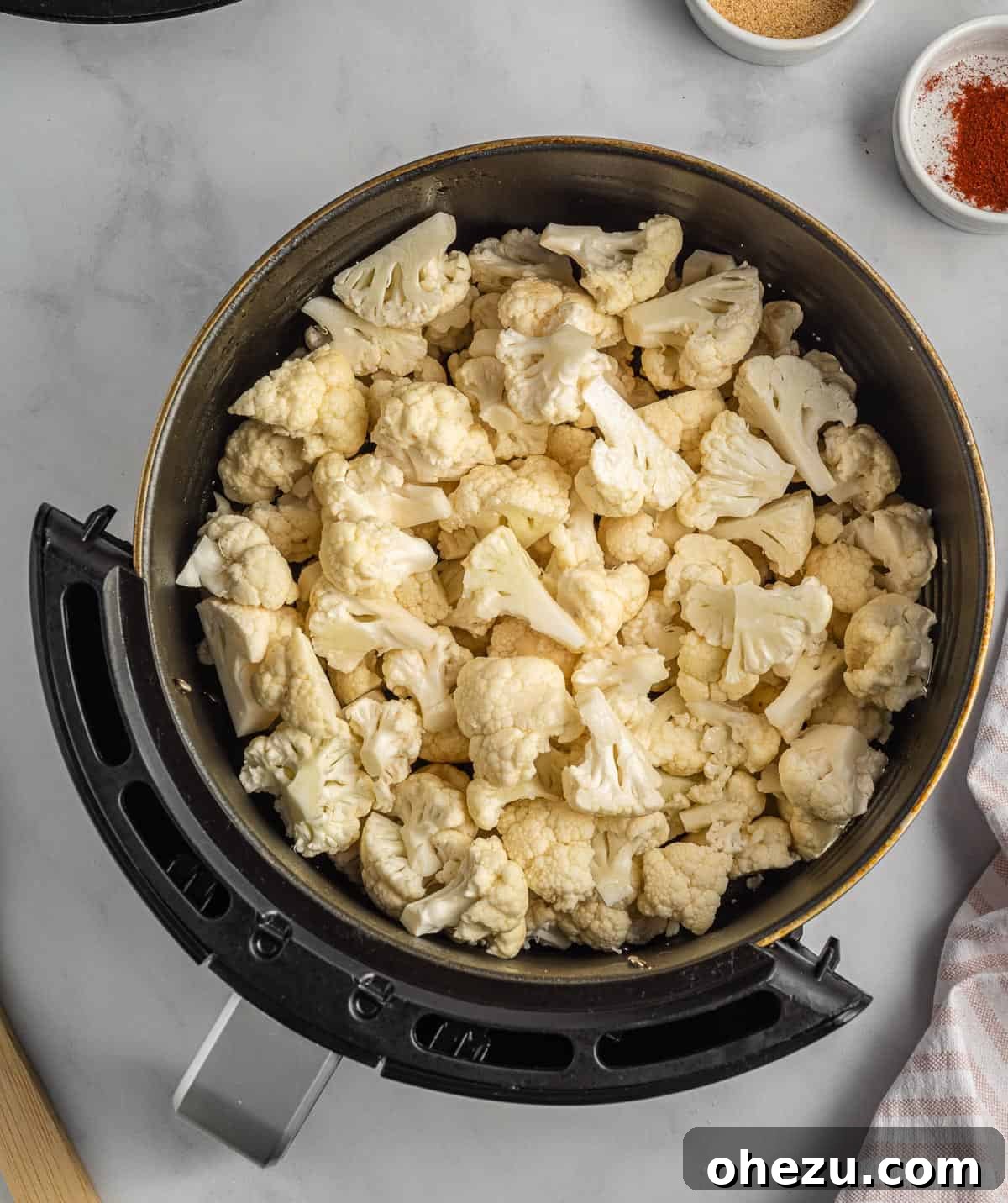 Cauliflower florets freshly placed into an air fryer basket, ready for seasoning.