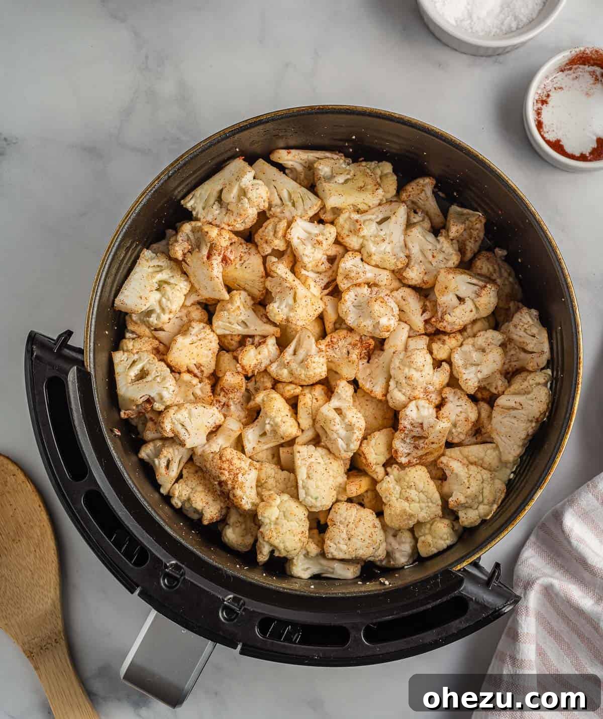 Cauliflower florets in the air fryer basket, now tossed with a blend of salt, garlic powder, and paprika.
