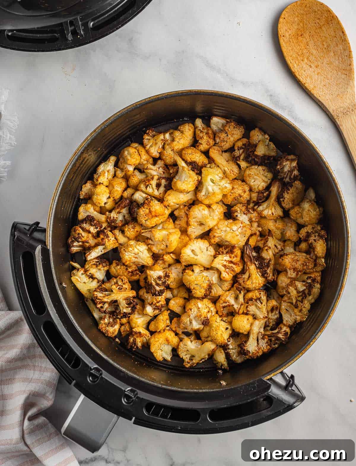 A closer view of the air fried cauliflower, glistening with seasoning, still in the air fryer basket.