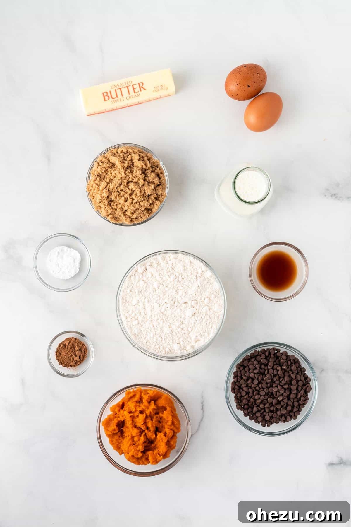 An array of fresh ingredients including canned pumpkin, flour, sugar, butter, and spices, neatly arranged and ready for baking mini pumpkin muffins.