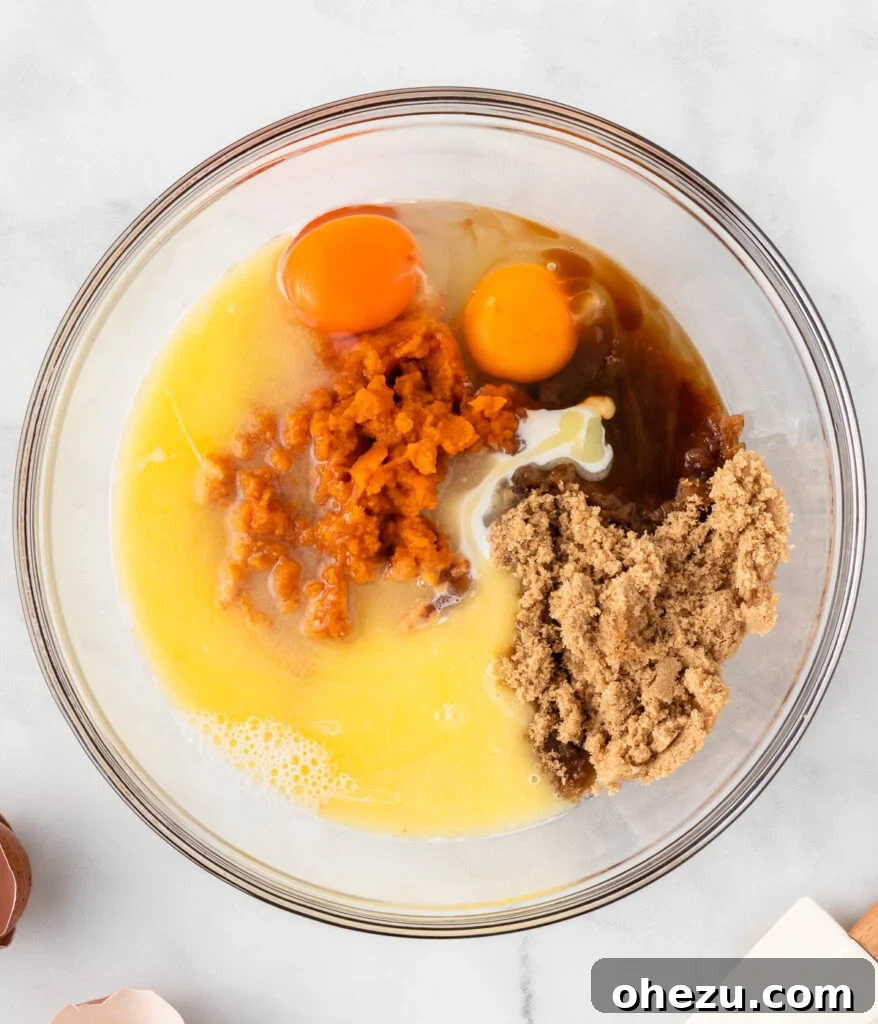 Various wet ingredients, including vibrant pumpkin puree and melted butter, resting in a mixing bowl before being combined.