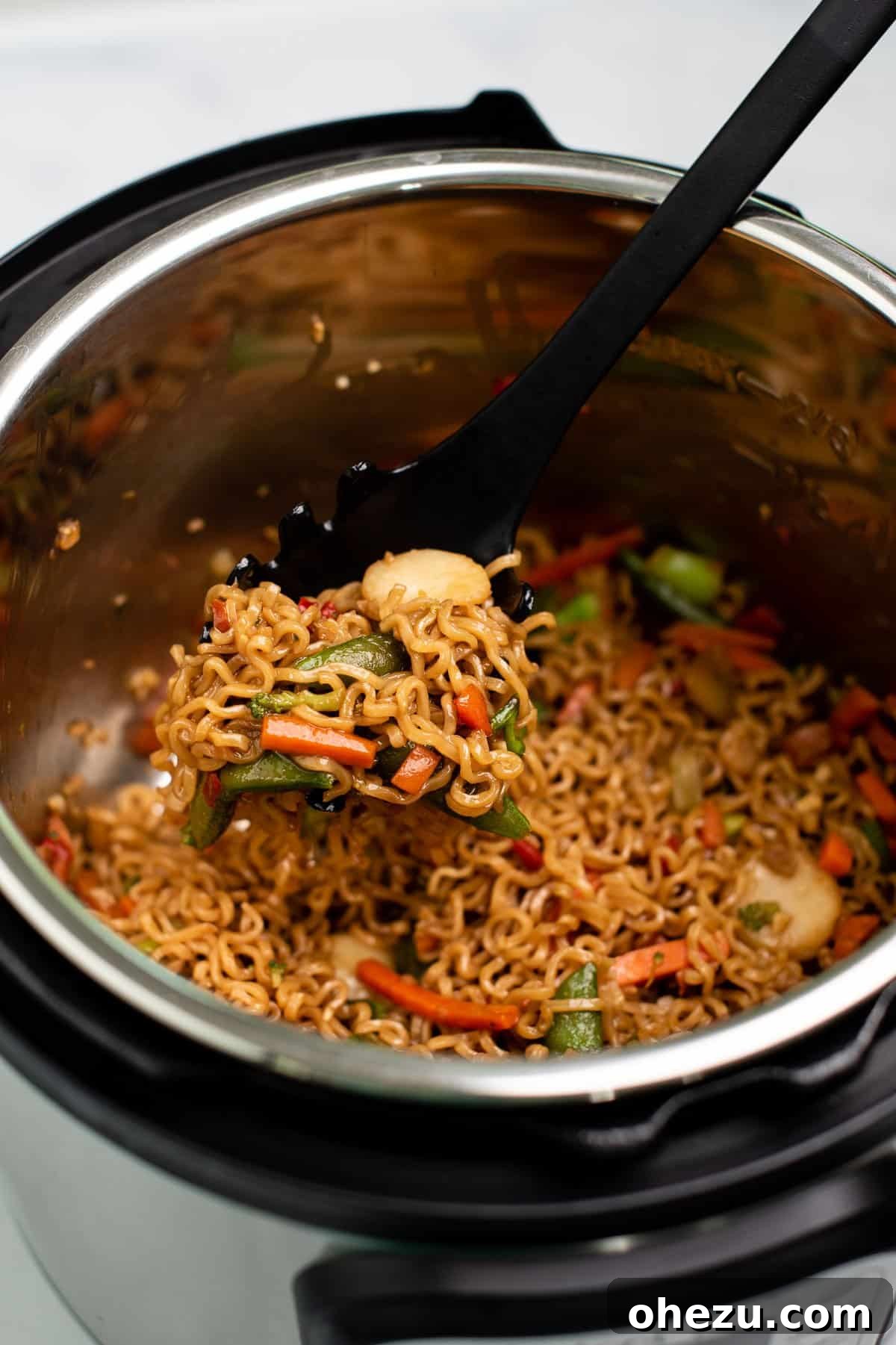 Scooping a serving of delicious ramen noodle veggie stir fry from an Instant Pot, showing steam and vibrant colors