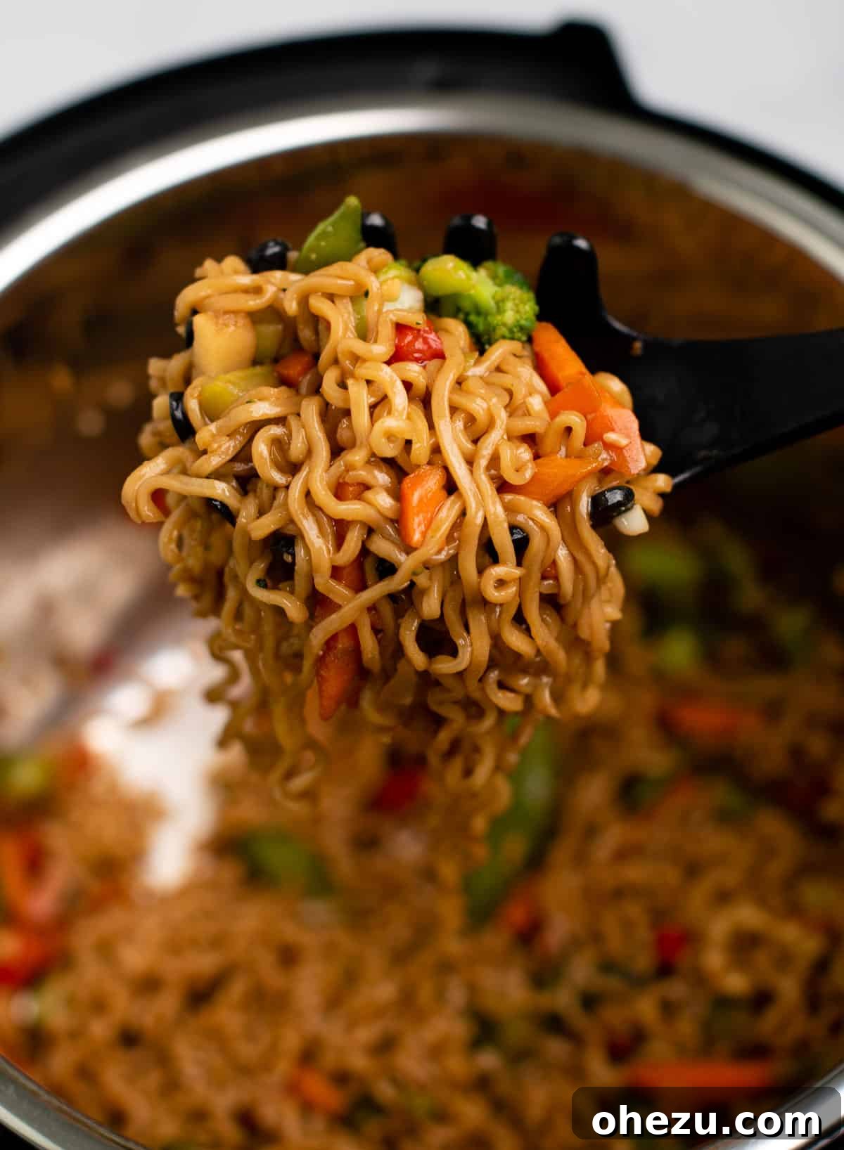 Close-up of Instant Pot stir fry being scooped out, showcasing perfectly cooked ramen noodles and colorful vegetables