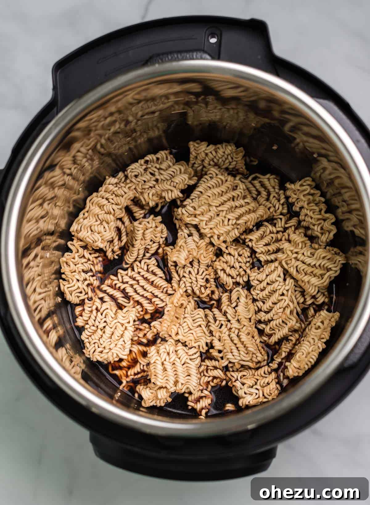 Pouring soy sauce and vegetable broth over ramen noodles and minced garlic in the Instant Pot