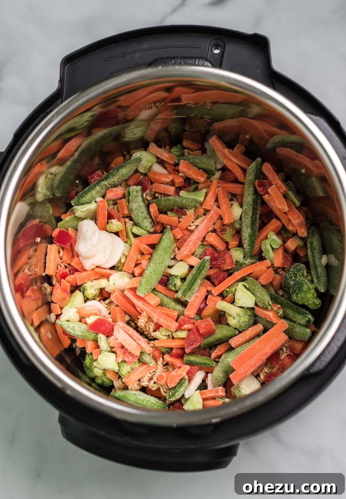 Frozen stir-fry vegetables completely covering ramen noodles in the Instant Pot insert