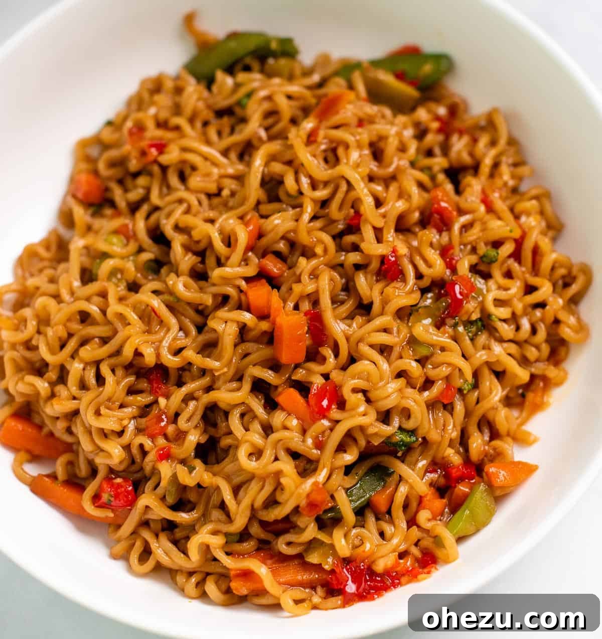 A vibrant bowl of Instant Pot ramen noodle stir fry topped with sweet chili sauce, fresh green onions, and sesame seeds, ready to be enjoyed.