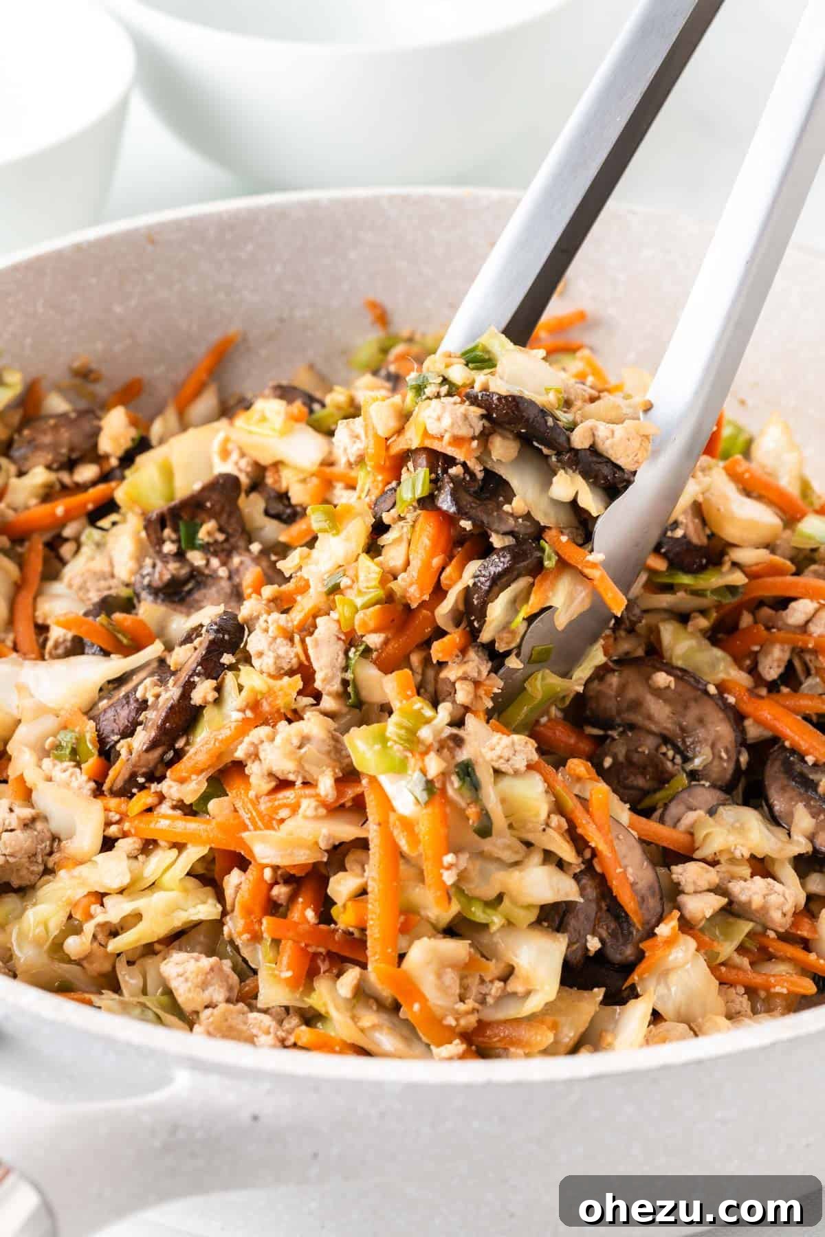 tongs taking egg roll filling from the skillet