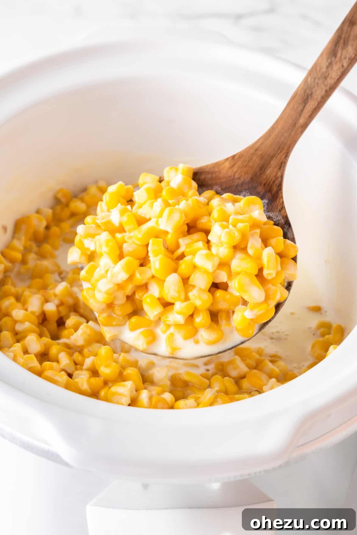A wooden spoon lifting a generous portion of finished slow cooker creamed corn from the crock pot, showing its rich texture.