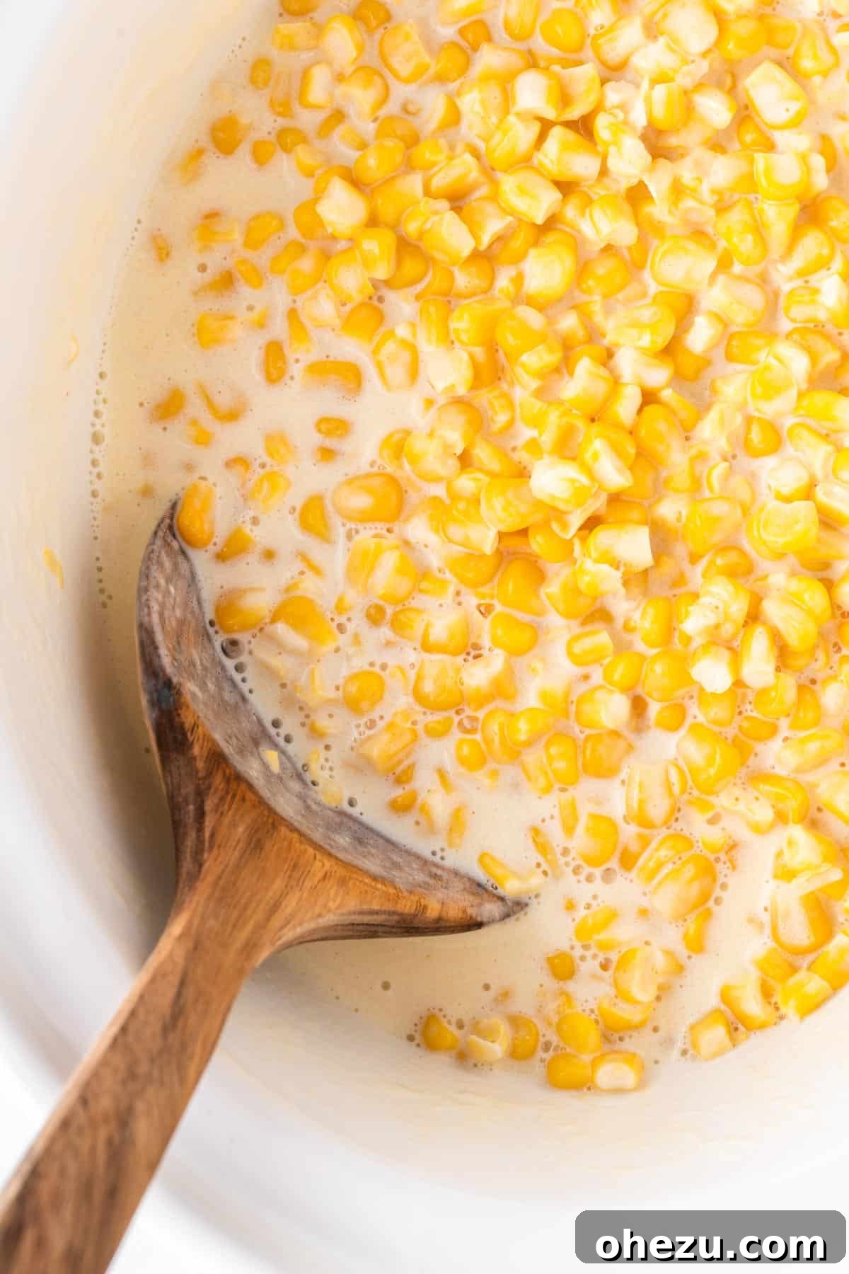 A wooden spoon scooping a generous portion of cheesy slow cooker creamed corn from the crock pot, highlighting its creamy texture.