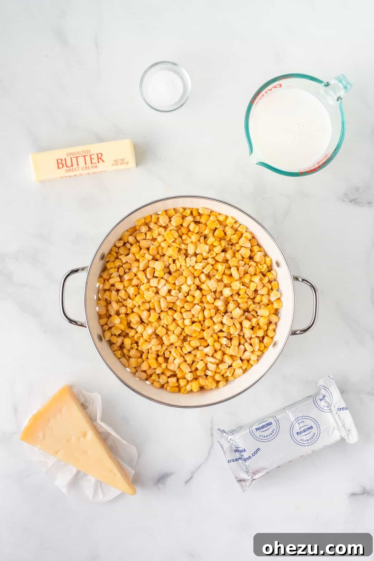All ingredients for slow cooker creamed corn laid out: frozen corn, cream cheese, butter, milk, salt, and a bowl of grated parmesan.