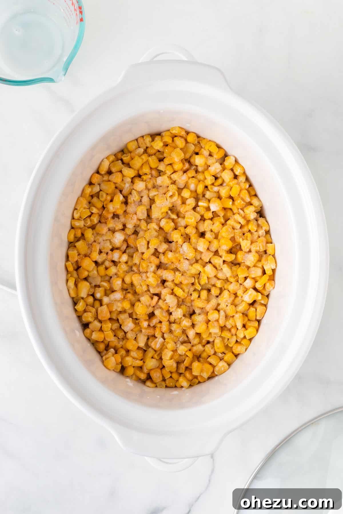 Frozen corn kernels added to a slow cooker, with milk poured over them and salt sprinkled on top.