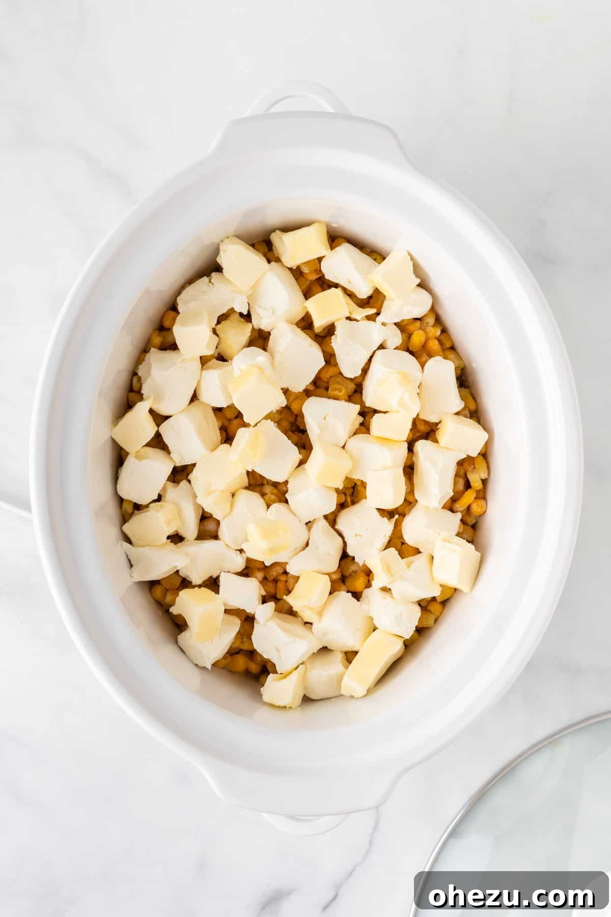 Slices of butter being added over the corn and cream cheese in the slow cooker before cooking.