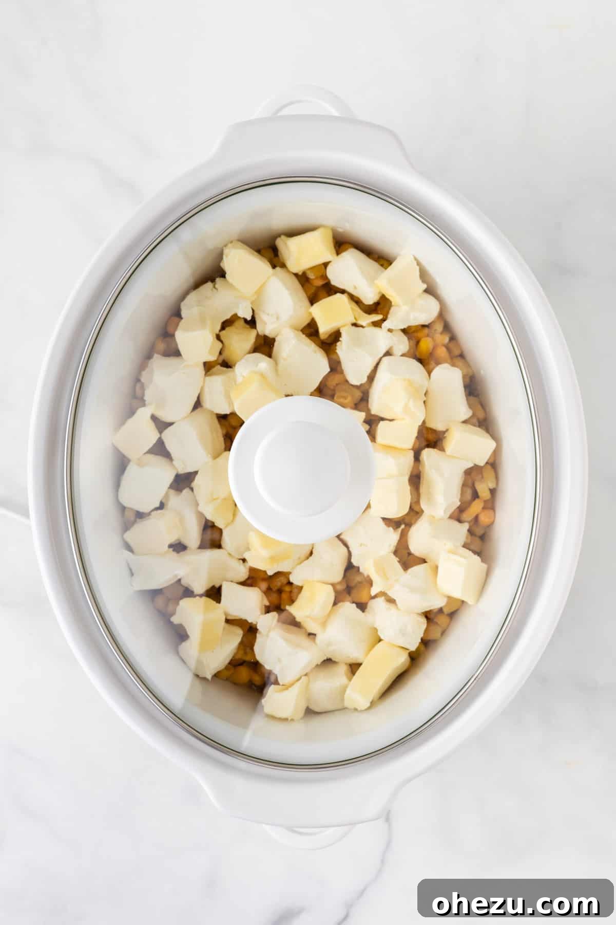 Lid being placed on the slow cooker filled with ingredients for creamed corn, ready to cook.