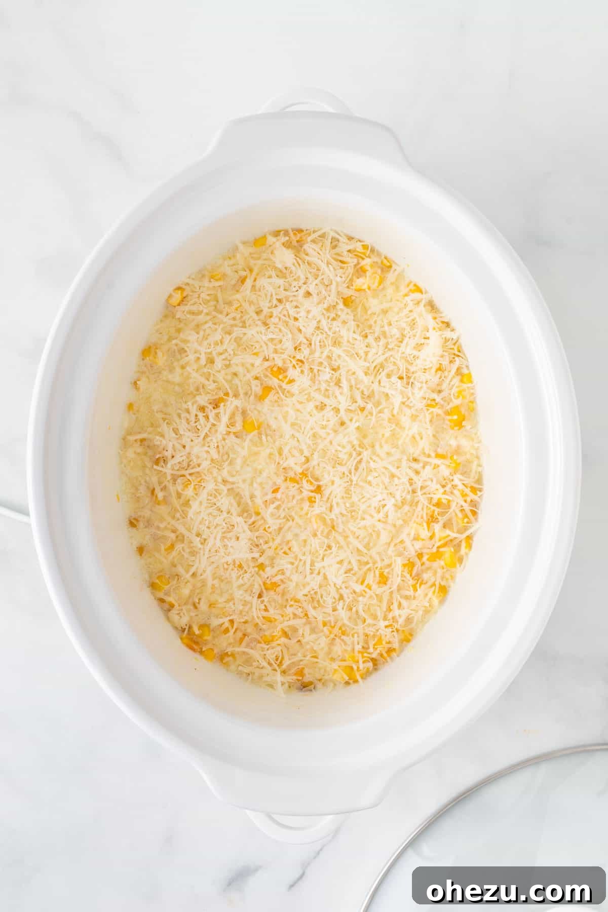 Freshly grated parmesan cheese being stirred into the hot, creamy slow cooker creamed corn.