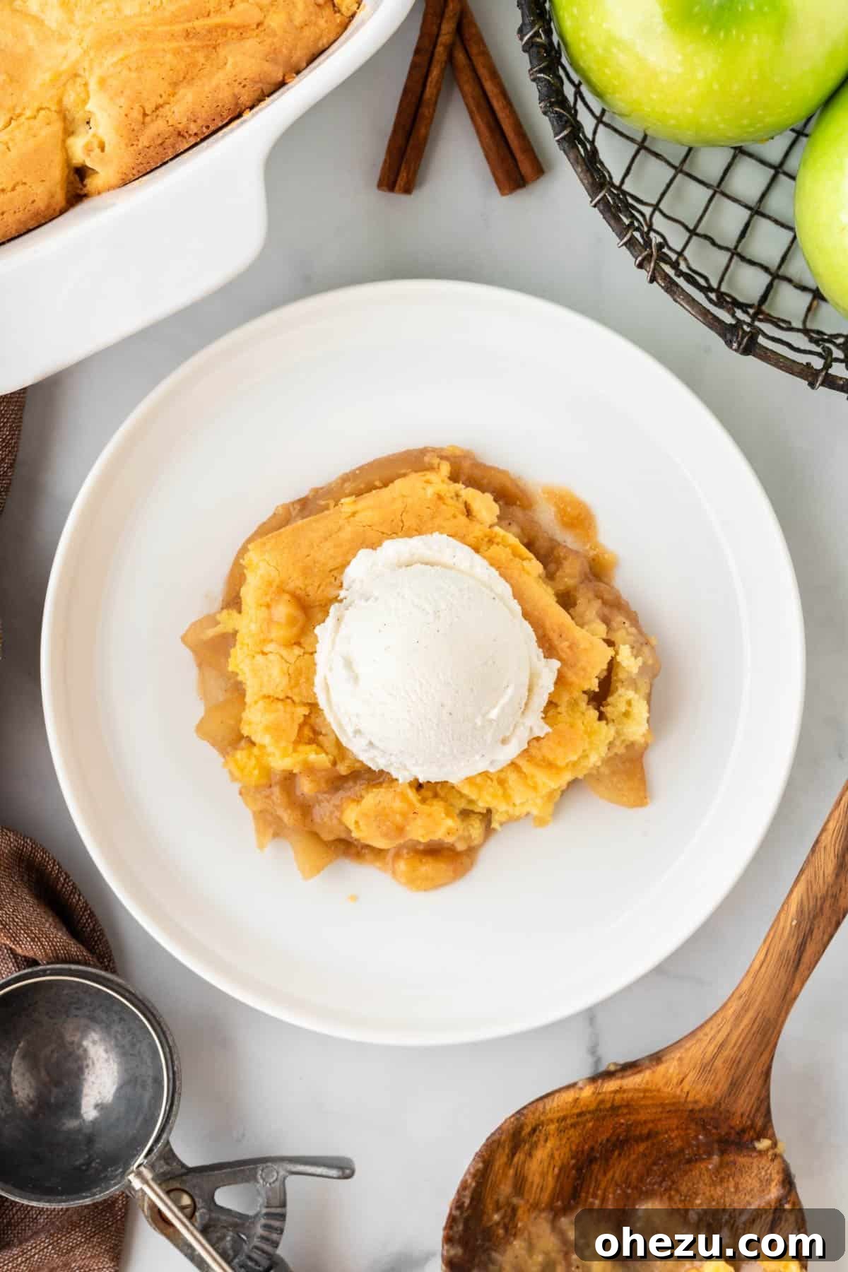 A close-up of a warm slice of cake mix apple cobbler on a plate, featuring tender apples and the golden cake topping, with a melting scoop of vanilla ice cream.