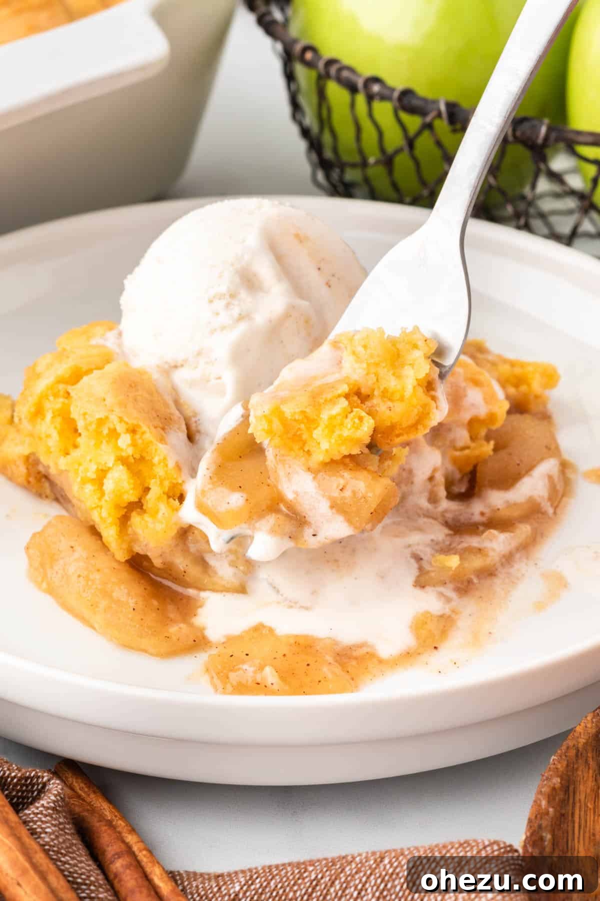 A fork taking a bite out of a warm piece of cake mix apple cobbler, showing the texture of the apples and the cake topping.