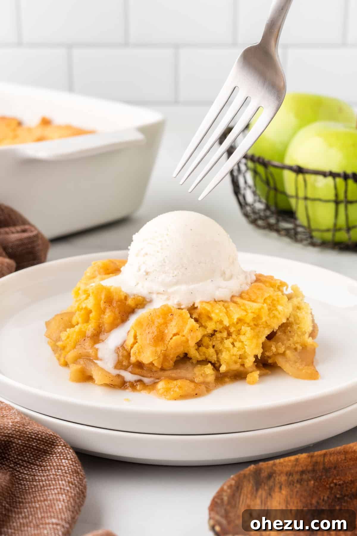 A beautifully composed shot of apple cobbler on a plate, featuring the golden crust, tender apples, and a generous scoop of melting vanilla ice cream with a subtle reflection.