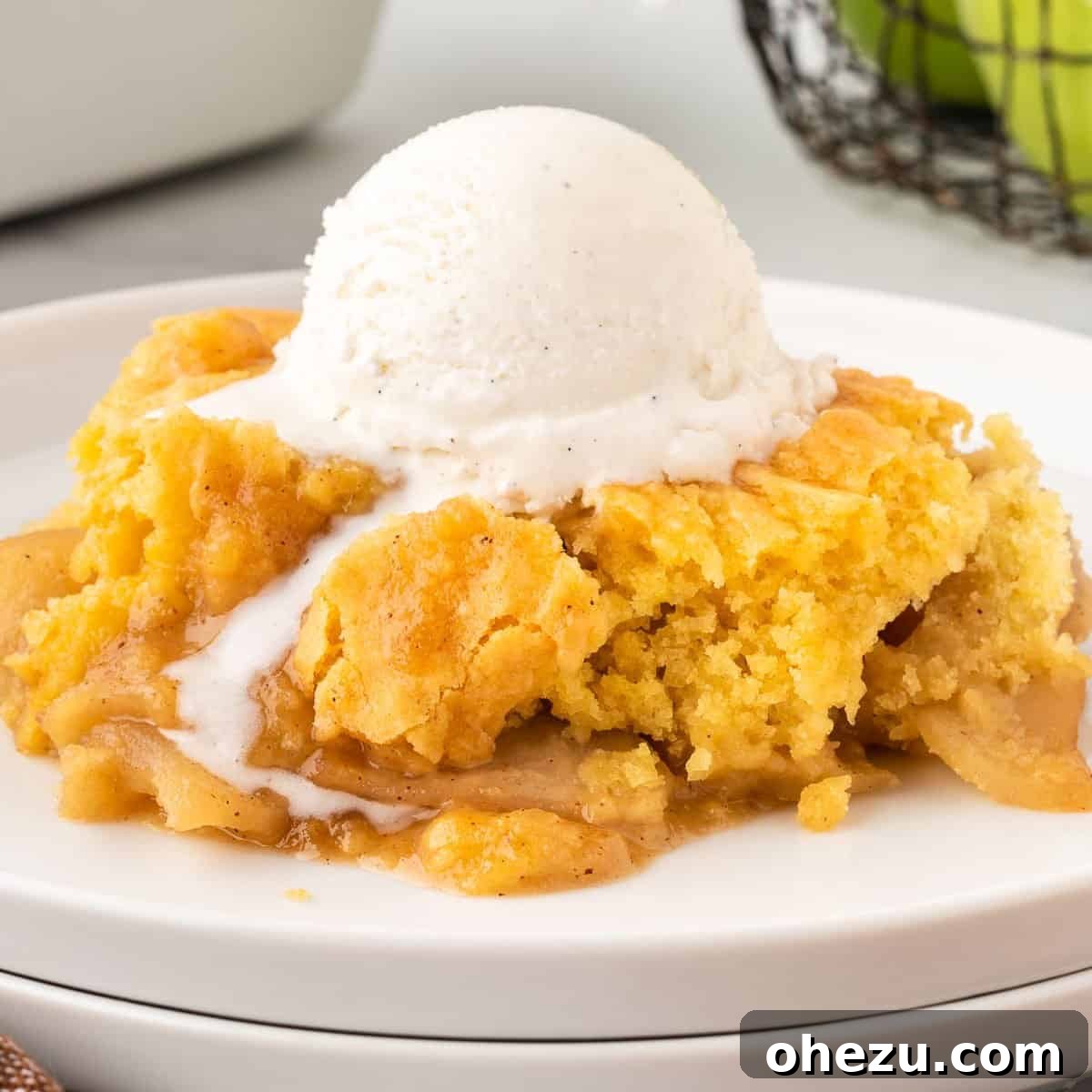 A close-up shot of a plate with a generous portion of apple cobbler, topped with a scoop of vanilla ice cream, against a rustic wooden background.