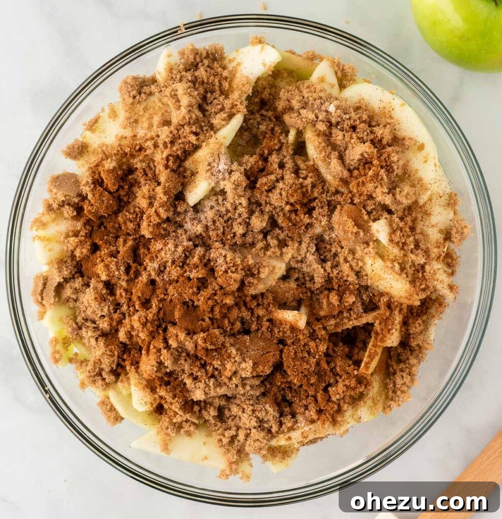 Close-up of sliced apples in a bowl, dusted with brown sugar, cinnamon, nutmeg, and salt, waiting to be mixed.