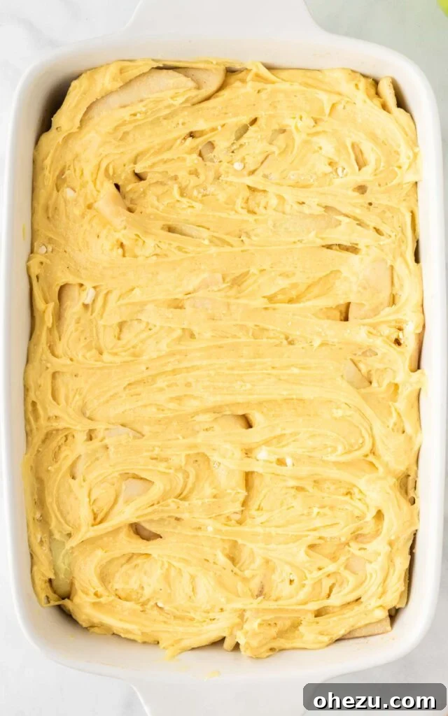 The cake mix batter being poured over the spiced apples in the baking dish, creating the topping for the cobbler.