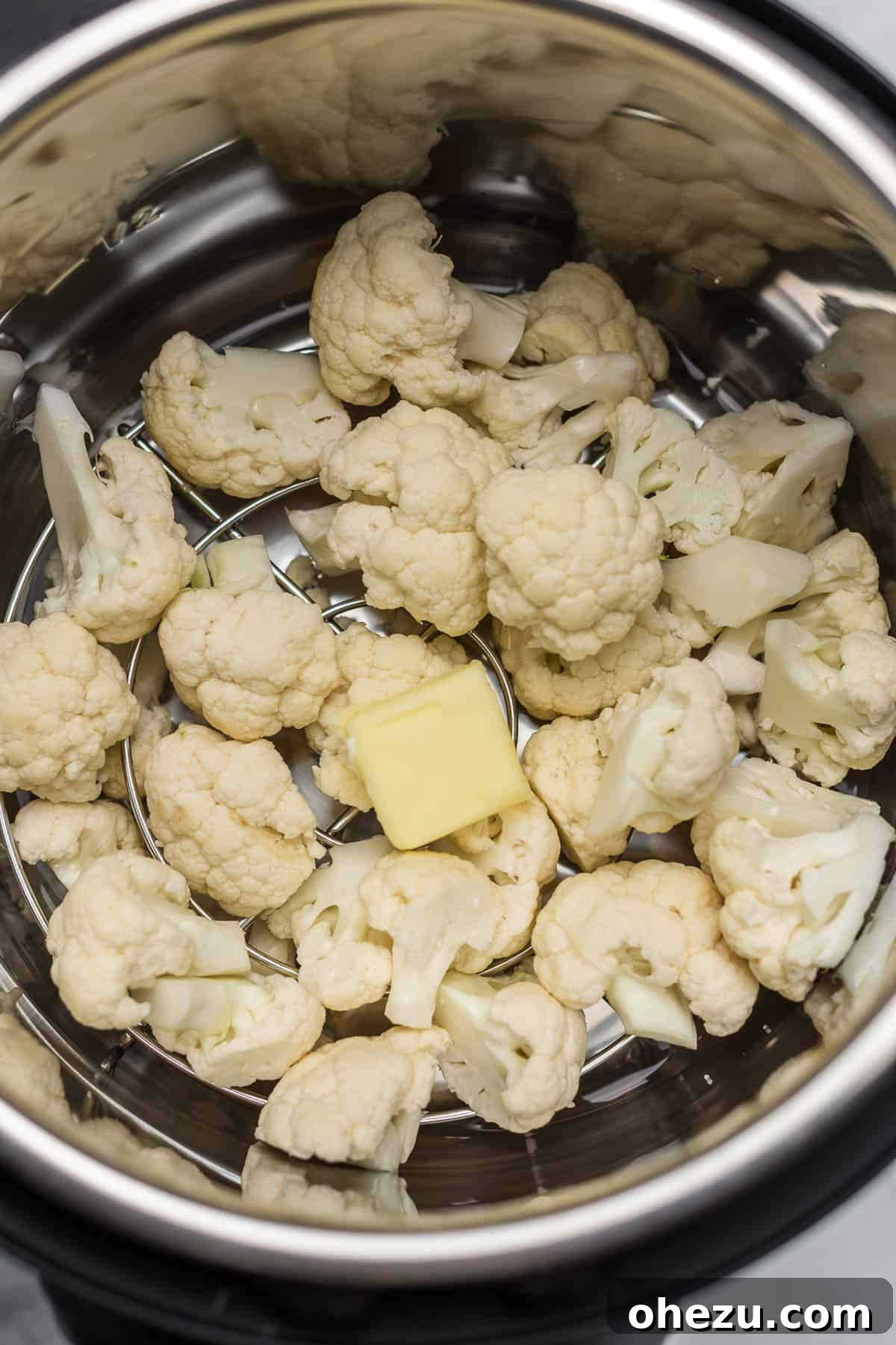 Cauliflower florets inside an Instant Pot with a pat of butter placed on top, before cooking.