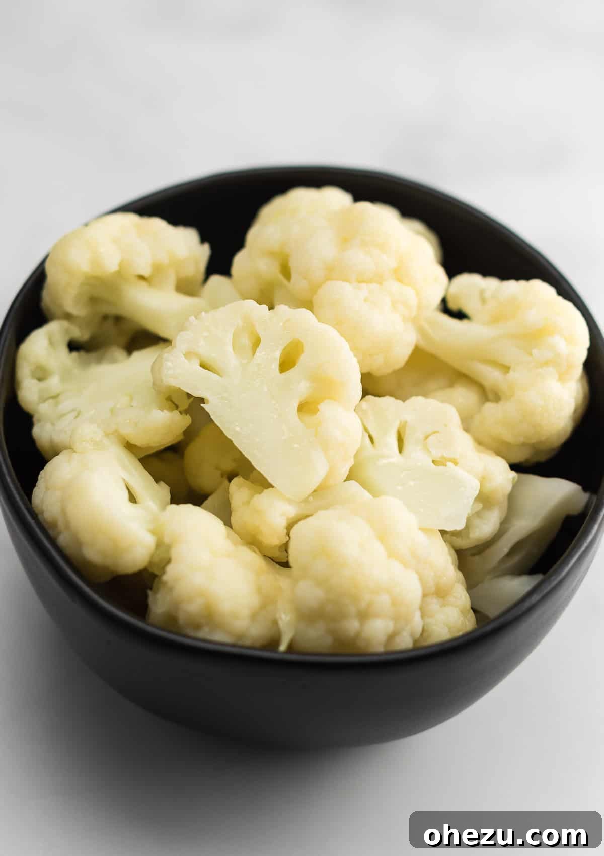 A bowl of hot, steamed cauliflower with melting butter and a sprinkle of salt.
