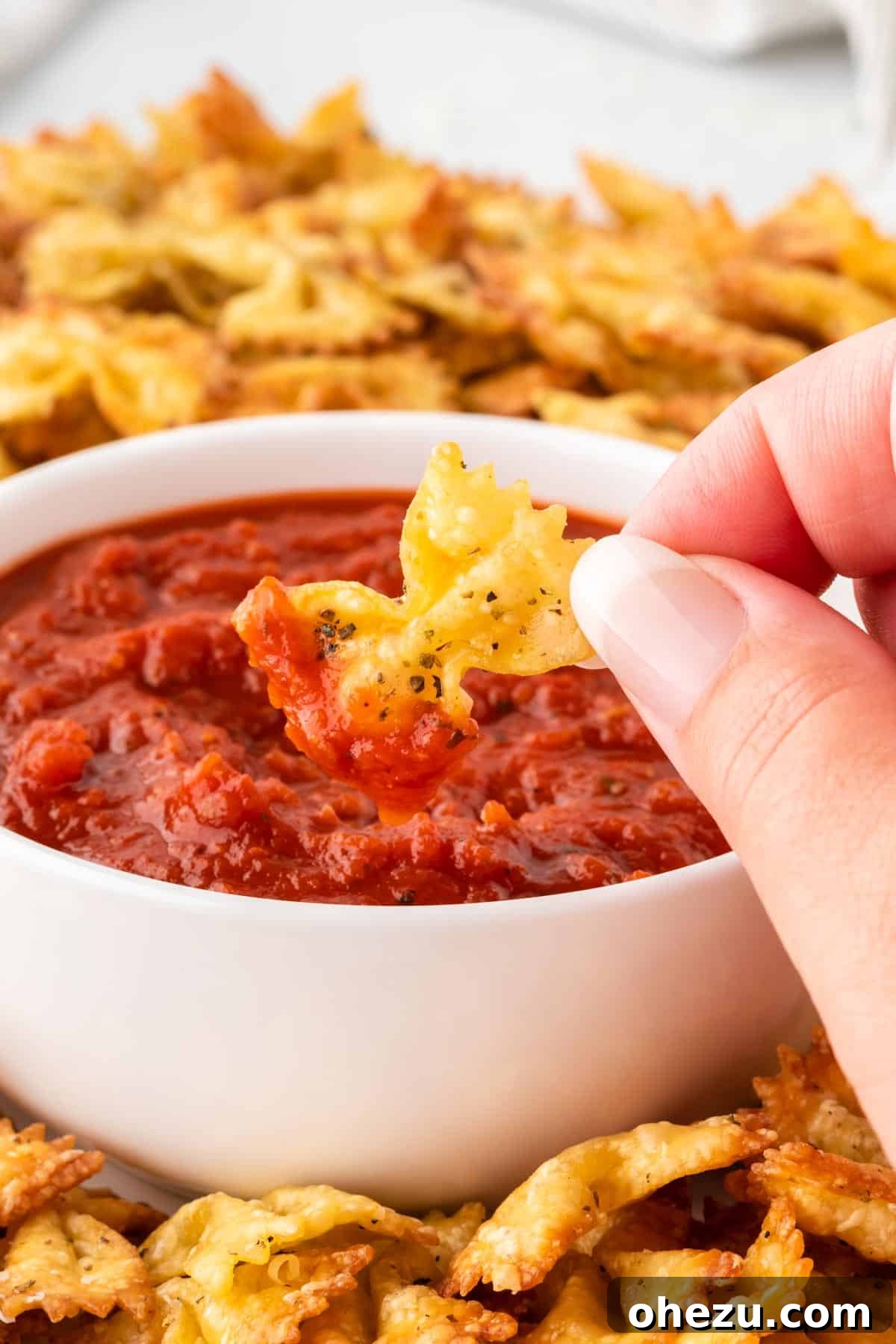 A crispy pasta chip being dipped into marinara sauce
